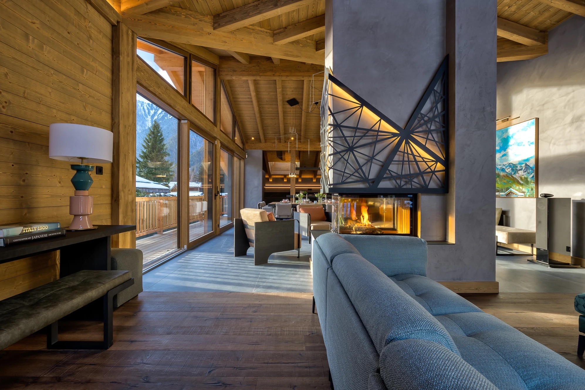 Cosy living room with central three-sided fireplace, mustard armchairs and floor-to-ceiling windows over the alpine valley
